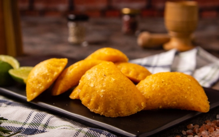 Empanadas de carne desmechada y papa crujientes servidas con ají y bebida refrescante.