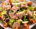Ensalada fresca con atún, tomate cherry, pepino y aceitunas en un plato blanco.