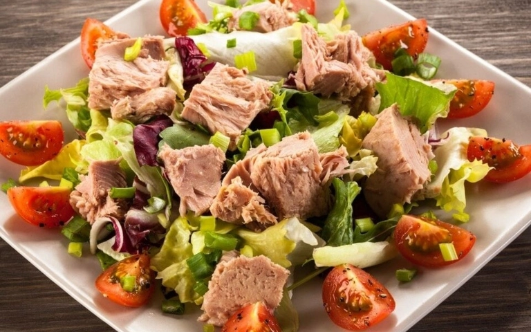 Ensalada fresca con atún, tomate cherry, pepino y aceitunas en un plato blanco.